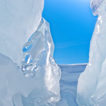 Narrow icy crevasse of glacier with some fresh snow and blue sunny sky visible in the opening
