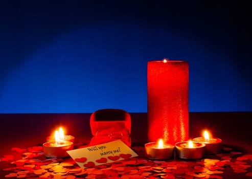 Two rings and a card with marriage proposal with six candles on the blue background