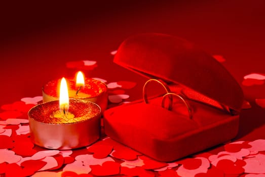 Two rings in a box and two candles over red background