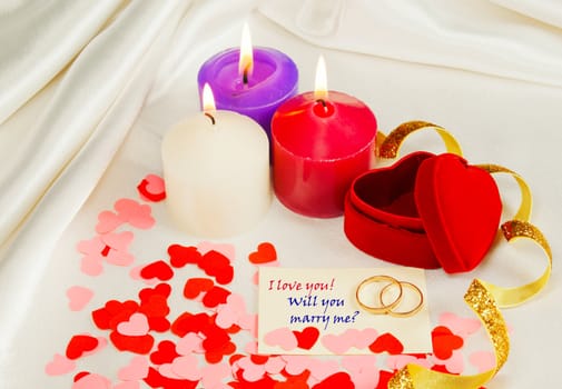 Two rings and a card with marriage proposal with three candles on the red background