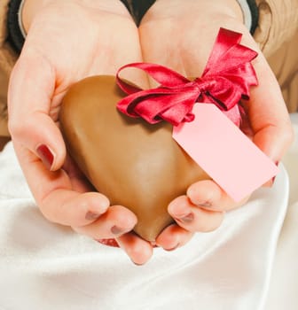 Hands holding a heart shaped chocolate candy 