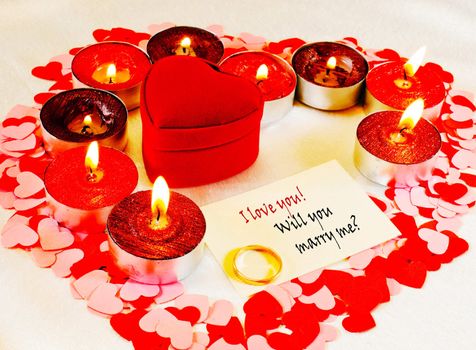 Ring and a card with marriage proposal with burning candles. Shallow depth of field.