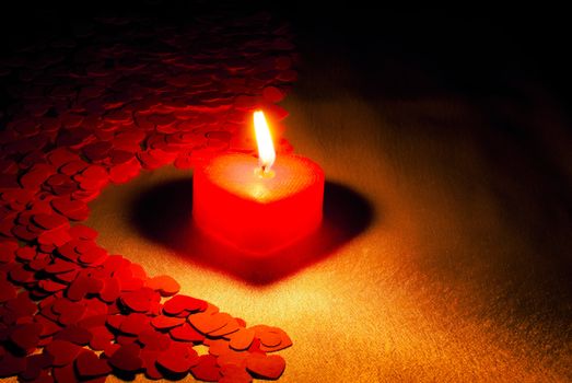 Burning heart shaped candle over red background