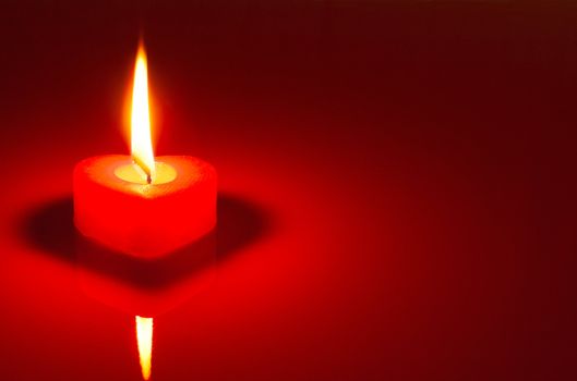 Burning heart shaped candle over red background