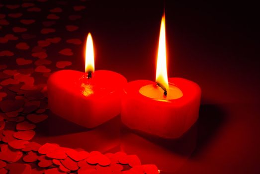 Two burning heart shaped candles over red background