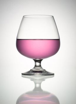 Pink wine in brandy glass and reflection on white table