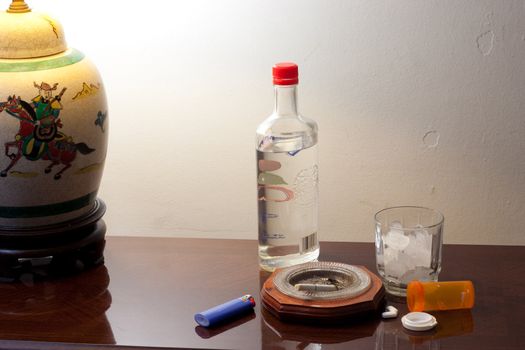 Pills, glass with ice and liquor bottle on coffee table ready to party