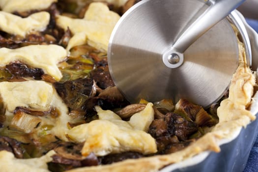 Mushroom and leek tart about to be cut with a pizza cutter.