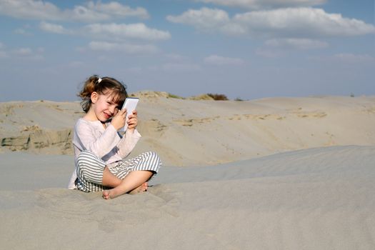 little girl sitting on sand and play with tablet pc