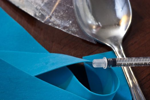 Close view of a syringe and blue tie off with spoon.
