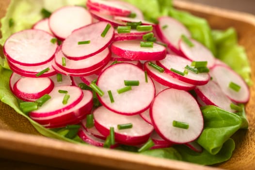 Fresh radish salad with chives served on a lettuce leaf on a wooden bowl (Selective Focus, Focus in the middle of the photo)