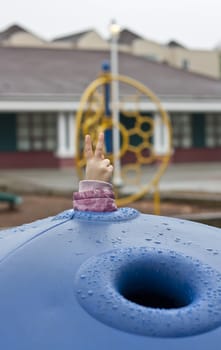 Child show gesture on playground at rainy day.