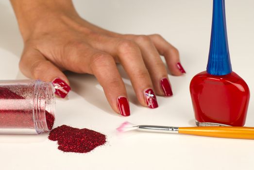 Hand with shiny red nails surrounded by nail art utensils