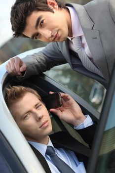 two young businessmen sitting in a car and talking on a cell phone