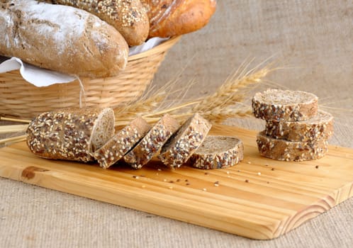 Diverse bread with slices of bread with grains on a wooden board with ears of wheat