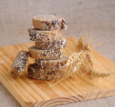 A stack of slices of bread with grains on a wooden board with ears of wheat 