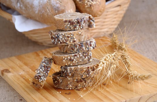 A stack of slices of bread with grains on a wooden board with ears of wheat