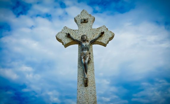 Religious Cross sculpture on blue cloud background.