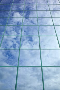 clouds and blue sky reflected in glass facade of office building