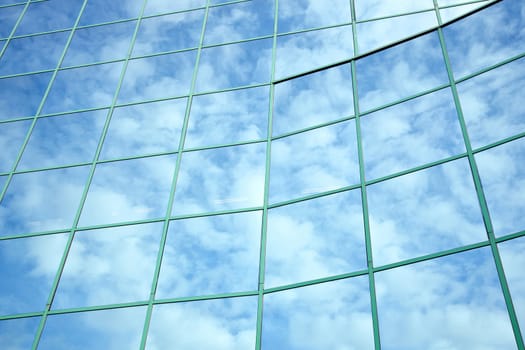reflections of blue sky and clouds in curved facade of office building