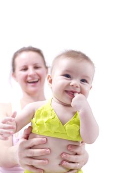 Baby in yellow bikini held by mother, she smiles while sucking her hands.