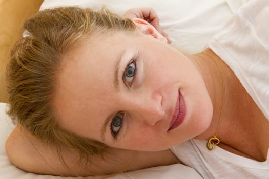 Blonde green eyed woman in the bed lying on her arm looking satisfied.