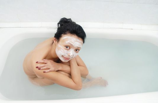 Pretty woman with beauty mask sitting in the bath