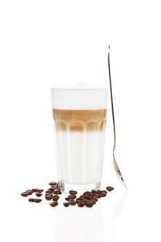 latte macchiato with a standing spoon and coffee beans on white background