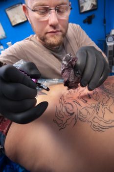 Bearded Caucasian tattooist creates a tattoo on a woman's back