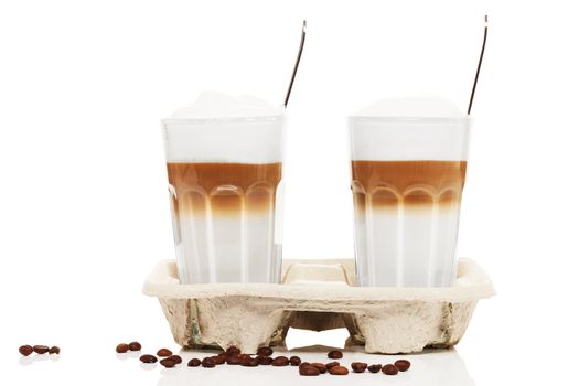 latte macchiato in a cupholder with coffee beans and spoons on white background