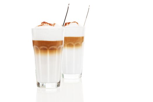 two glasses latte macchiato with chocolate powder and spoons inside on white background