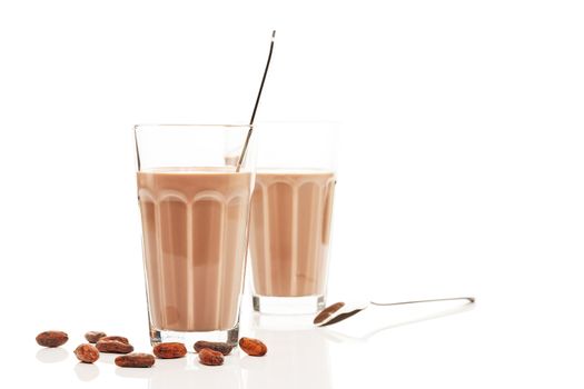 chocolate milk in front of other chocolate milk with chocolate beans and spoons on white background