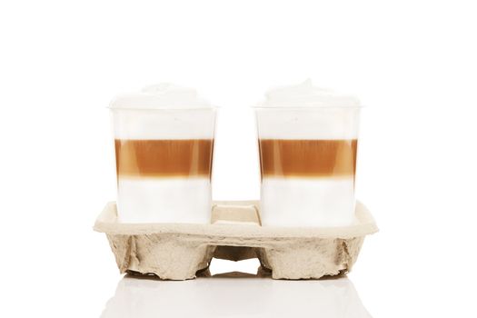 two plastic cups with latte macchiato to go in a cupholder on white background