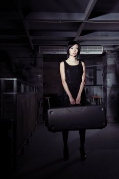 Small brunette lady holding big suitcase in the dark airport terminal