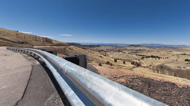 A wide angle shot of a curving road overlooking Cripple Creek, Colorado with snow capped mountains in the distance.