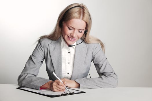 business woman in a headset writing in notebook