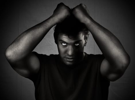 Black and white photo of a young handsome man looking at the camera with muscular hands gripping his hair.