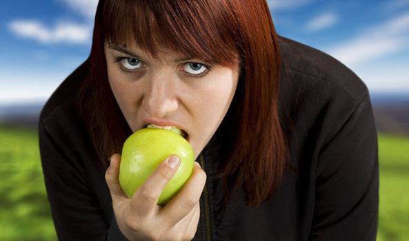 Redhead girl biting on a delicious green apple with a flirtatious look.

Shot in studio.
