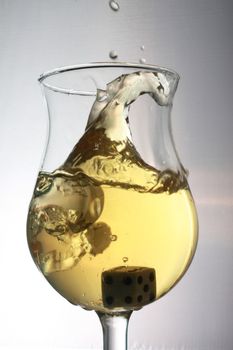 Dice being dropped and splashing into a glass of white wine.