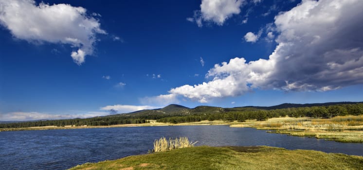 A wide angle high dynamic range image of a lake with mountains and blue sky in the background.