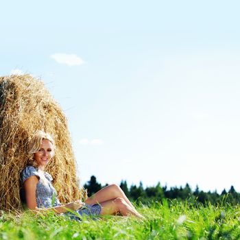 portrait of a girl next to a stack of hay under the blue sky