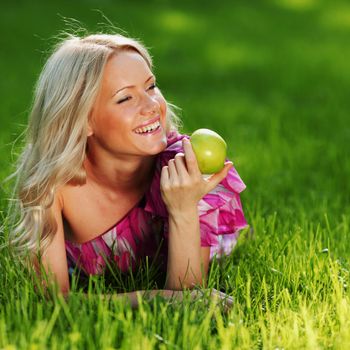 blonde holding an apple in his hand lying on green grass