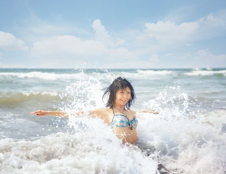 Happy lady playing with water and waves in the summer sea