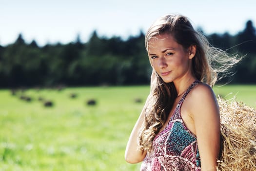 portrait of a girl next to a stack of hay under the blue sky