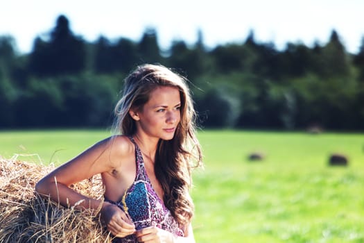 portrait of a girl next to a stack of hay under the blue sky