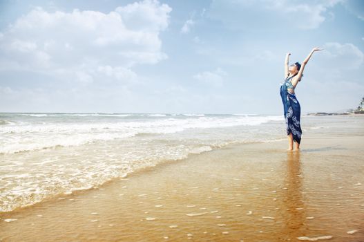 Happy lady standing in the water with hands up. Summer beach in Goa, India. Horizontal photo with vibrant colors