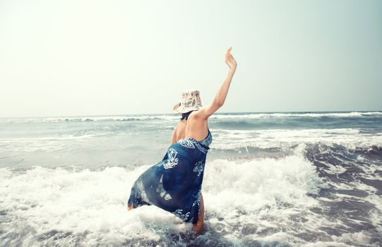 Happy lady in hat playing with waves at the sea