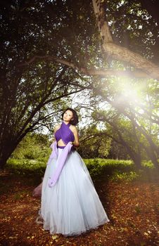 Elegant lady in the fairy autumn forest with sunlight at the background