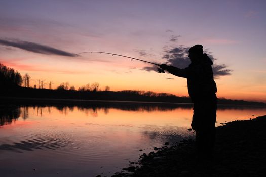 Silhouette of the fisher on a background of an evening dawn