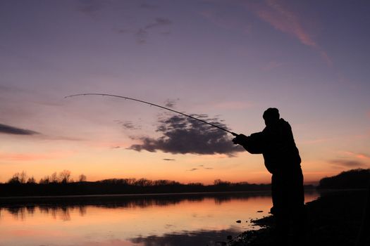 Silhouette of the fisher on a background of an evening dawn